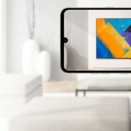 Phone held up in a living room, showing a 4K TV displaying an abstract orange and blue painting on the wall, with an LG TV WebAR label and QR code