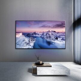 The LG 75UR80006LJ wall mounted in a concrete walled room, showing a snow covered coastline on screen