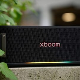 Front view of the black xboom Bounce speaker on a concrete ledge, its lower edge lit in green, yellow and orange